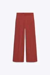 Pantalón color ladrillo de corte palazzo, con bolsillos laterales y traseros, detalle de pliegues en el frente y cierre frontal con cremallera, botón interior y gancho metálico. Confeccionado en hilatura con 21% de lino.
