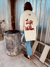 Sweater tejido en lana color crudo, con cuello alto, corte holgado y bordado a mano en color rojo con la frase "Life Walker" en la espalda.