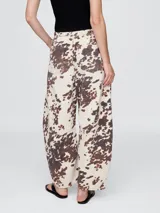 Pantalón jean tiro alto, corte amplio y estampado animal print de vaca en tonos marrones y blancos.