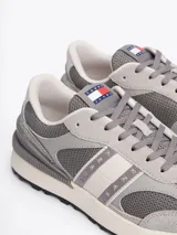 Zapatillas Tommy Jeans grises de corte bajo, con exterior de ante y malla, detalles distintivos de la marca, suela de goma dentada y cierre con cordones.