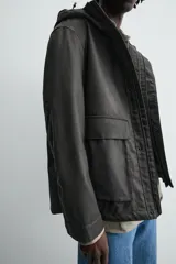 Parka relaxed fit color negro confeccionada en tejido de lino que repele el agua. Tiene cuello con capucha ajustable, mangas largas con puños abotonados, bolsillos frontales con solapa y cierre frontal con cremallera oculta por solapa con botones a presión.
