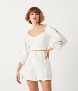 Blusa corta blanca de algodón con escote cuadrado, manga larga abullonada con bordados, y látex en la espalda.