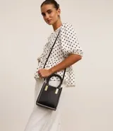 Bolso transversal pequeño tipo bandolera, color negro con detalles en blanco y herrajes dorados. Tiene correa de mano, asa larga desmontable y cierre superior.