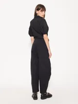 Pantalón negro de poplin 4way con lazo en la cintura, bolsillos ojales en delantero y espalda, pinza a la altura de la rodilla que le da una forma curvada, acceso mediante broche pantalonero, cierre y botón interno a tono de tela. Broches en el ruedo permiten ajustarlo.