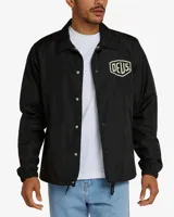 Campera negra tipo coach con cierre de botones a presión, bolsillos laterales y logo de la marca Deus Ex Machina estampado en el pecho.