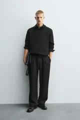 Pantalón negro de corte relajado con cintura elástica ajustable y pliegues en la parte delantera. Presenta bolsillos laterales y bolsillos traseros de parche.