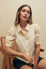 Camisa color crema de mangas cortas abullonadas con calados florales en las mangas.