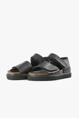 Sandalia plana negra de cuero, con tiras anchas cruzadas y ajuste con velcro.