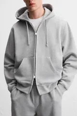 Sudadera negra relaxed fit de algodón compacto con interior en rizo, cuello con capucha ajustable, manga larga, bolsillos frontales tipo canguro, acabados en rib y cierre frontal con cremallera.