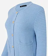 Cardigan de punto blanco, con cuello redondo, manga larga y cierre frontal de botones dorados. Posee dos bolsillos cuadrados en la parte delantera inferior.