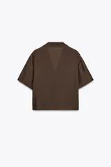 Camisa marrón de cuello solapa y escote pico con manga corta. Bolsillos de plastrón en pecho. Cierre frontal con botones.