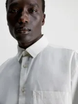 Camisa blanca de corte relaxed con cuello en punta, cierre de botones y bolsillo de parche en el pecho, hecha de mezcla de algodón y lino.