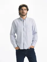 Camisa celeste y blanca a rayas verticales, de manga larga y corte clásico. Tiene cuello abotonado y bolsillo en el pecho.