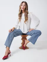 Blusa blanca de gasa plisada con encaje calado en el cuello y el pecho. Cuello a la base fruncido, manga larga con puño elastizado y espalda lisa con abertura tipo gota y botón.