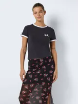 Camiseta negra de corte cropped con cuello redondo y mangas cortas con ribete blanco. Estampado pequeño de moño blanco en el pecho.
