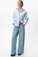 Camisa celeste y blanca a rayas verticales, de corte recto, con cuello solapa, escote pico y manga larga. Cierre frontal con botones.