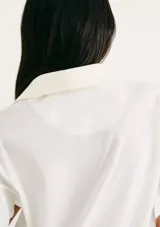 Camiseta blanca de manga corta con cuello polo profundo y holgada. Presenta un pequeño logo bordado en el pecho.