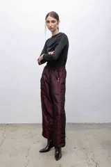 Pantalón de tafeta tornasolada color borgoña, de corte recto con cintura elastizada, bolsillos frontales con cierre plateado, y cordones ajustables en las pantorrillas para fruncir el bajo.