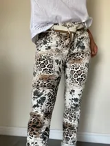 Pantalón de mujer con estampado animal print y detalles florales en tonos beige y negro, de corte recto y con ruedo doblado. Incluye un cinturón de tela beige y marrón.
