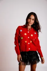 Saco de punto color rojo, con cuello polo y cierre frontal de botones blancos. Presenta flores bordadas en relieve de diferentes colores (azul, amarillo, verde, naranja, rosado) y mangas largas con diseño de burbujas.