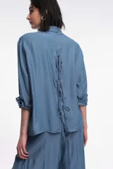 Camisa color marrón de corte holgado, con cuello clásico, mangas largas con puños abotonados y cierre frontal con botones. 