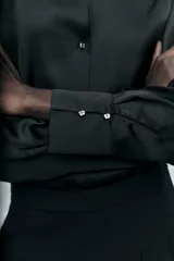 Camisa azul marino de satén con cuello solapa, escote en pico y mangas largas con puños abotonados.