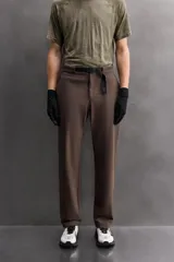 Pantalón de hombre color beige/caqui, de corte regular fit, confeccionado en tejido técnico compacto con elasticidad. Presenta cintura ajustable con cinturón a contraste, bolsillos frontales, bolsillo trasero con cierre de cremallera oculta y bolsillo cargo con cierre de cremallera oculta en la pernera.