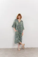 Vestido midi verde con estampado de hojas azules y blancas, corte amplio, cuello camisero, mangas 3/4 y bolsillos laterales.