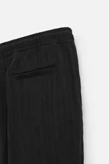 Pantalón negro de corte amplio, con textura acanalada, cintura elástica ajustable con cordón, bolsillos laterales y traseros de vivo.