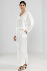 Camisa blanca de lino con botones, mangas largas con puños elásticos y dobladillo curvo.