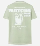Remera de manga corta, cuello redondo y calce oversized, color verde claro con efecto lavado. Presenta un estampado serigráfico en la espalda con un vaso de bebida helada y texto que dice "i'm powered by MATCHA FUEL ONLY daily clean energy CLUB".