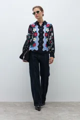 Camisa de manga larga, color azul marino, con estampado floral en tonos rojo, blanco y celeste. Presenta un diseño frontal con paneles ondulados en color celeste claro.