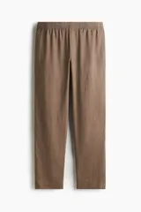Pantalón marrón claro de lino, corte recto, con cintura elástica y cordón ajustable. Posee bolsillos laterales y trasero.