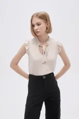 Blusa sin mangas color crudo con cuello con lazo y volados en los hombros.