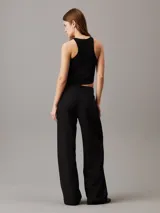 Top sin mangas negro de punto de rayón suave con sutil efecto brillante y bajo asimétrico. Diseño con espalda cruzada y bordado de Calvin Klein en la misma gama de tonos en el bajo.