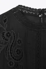 Blusa negra de algodón con cuello redondo y manga corta abullonada. Presenta bordados a tono y cierre en la espalda con abertura y botón.