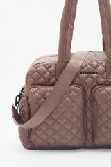 Bolso marrón con diseño matelassé, doble asa corta, correa larga desmontable y dos bolsillos frontales. Incluye llavero de corazón y dijes desmontables.