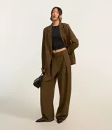 Pantalón de vestir color marrón, de corte amplio tipo barrel, con cintura lisa, cierre desplazado y pliegues delanteros.