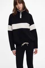 Buzo negro de polar con franja horizontal blanca, cuello alto con cierre y cintura con cordón.