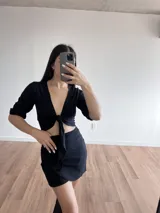 Conjunto negro de dos piezas compuesto por un top corto con escote en V y mangas cortas anudado en el frente y una minifalda con lazo en la cintura.