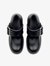 Zapato tipo Mary Jane de cuero negro, con suela track gruesa y dentada, y taco ancho. Presenta una tira ancha acolchada sobre el empeine con una hebilla metálica grande y plateada.