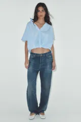 Camisa color gris claro con cuello solapa y escote pico, de manga corta. Presenta un nudo en la parte delantera y cierre frontal con botones.