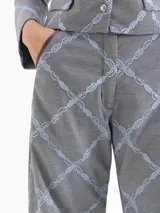 Pantalón de corte mom fit confeccionado en tejido con diseño de microcuadros y bordado de labios en color celeste que forman un patrón de rombos. Presenta una cintura con efecto de cinto integrado, bolsillos laterales con detalles en cuero color borravino y pinzas en las rodillas que aportan volumen. El cierre es mediante gancho, botón interno y cremallera.