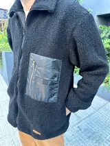 Campera de hombre color crema, de textura peluda, con cierre frontal, cuello alto, bolsillos laterales y un bolsillo impermeable negro en el pecho.