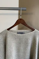 Poncho color beige con diseño a cuadros, cuello bote y terminaciones desflecadas. Tiene aberturas para los brazos en los laterales y detalles en cuero.