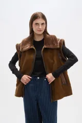 Chaleco marrón de gamuza sintética con cuello y borde de piel sintética. Cierre frontal con cremallera y bolsillos laterales.