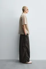 Pantalón cargo de corte ancho y relajado, color verde oscuro o negro, con cintura elástica, bolsillos laterales de parche y bolsillos traseros de vivo. Presenta pliegues verticales marcados en la parte delantera y cordones ajustables en los bajos.