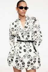 Vestido corto de algodón color crema con estampado floral negro, cuello mao, escote en V, mangas globo con puños elásticos, falda balloon y cinturón extraíble con hebilla ovalada.