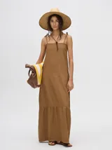 Vestido midi de denim algodón color marrón, con escote recto y tirantes finos ajustables con lazos. El corte es suelto y termina con un ruedo con semi-volado.