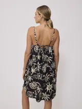 Vestido corto negro con estampado de palmeras, soles y estrellas en color crema. Diseño suelto con breteles finos y escote recto con lazo ajustable.